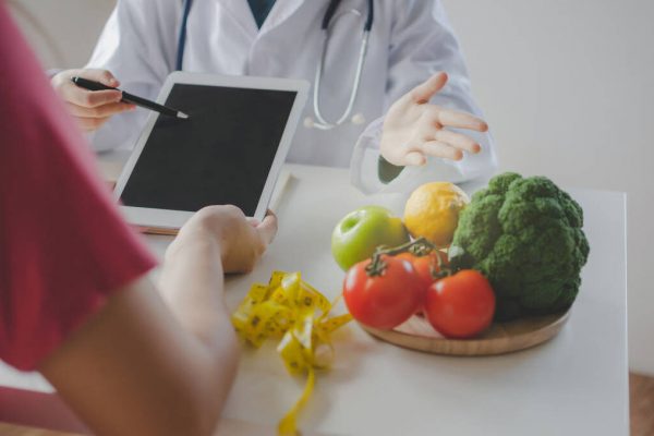 gesundenberatung (1) friendly nutritionist female doctor or medical using tablet and talking about diet plan with patient on desk at laboratory room at office hospital, food science, healthy food and dieting concept