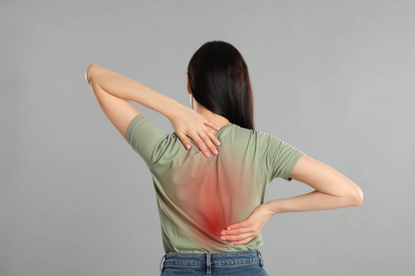 Woman suffering from pain in back on light grey background. Visi Woman suffering from pain in back on light grey background